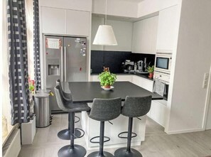 Eine moderne Küche mit einer zentralen Kochinsel, Barhocker, einer Hängeleuchte und einem Kühlschrank.