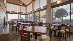 A spacious indoor dining area with multiple tables and chairs, large windows, and a brick wall. - Red Roof Inn & Suites Irving - DFW Airport South (Irving)