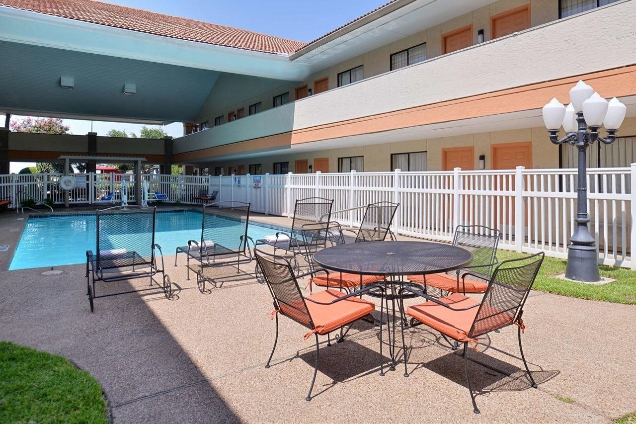 An outdoor pool area with a covered seating area, a fenced pool, and a building with multiple windows.