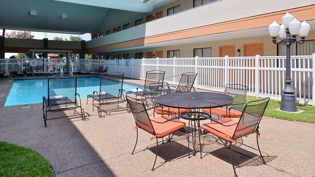 An outdoor pool area with a covered seating area, a fenced pool, and a building with multiple windows. - Red Roof Inn & Suites Irving - DFW Airport South (Irving)