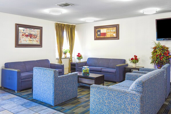Een hotelkamer met een blauwe gestreepte zithoek, een flatscreen televisie aan de muur en een lijst met een Texas vlag.