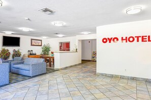 Un hall de hotel con mostrador de recepción, zona de estar y una pared con el nombre del hotel.