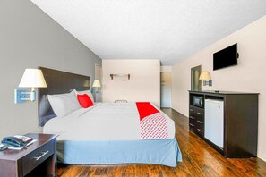 A hotel room with a bed, bedside lamps, a desk with a telephone, a television, and a refrigerator. - OYO Hotel Irving DFW Airport South (Irving)