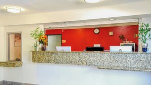 A reception desk with a red wall, a clock, and a computer monitor. - Americas Best Value Inn Irving Dfw Airport South (Irving)
