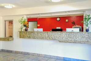 Un mostrador de recepción con pared roja, un reloj y un monitor de computadora.