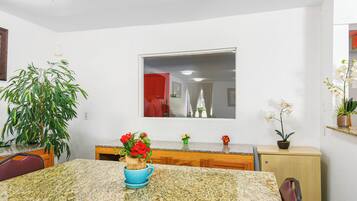 A kitchen with granite countertops, a dining table, chairs, a potted plant, and a mirror above the sink.