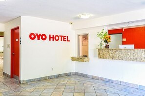 Zona de recepción de un hotel con una puerta roja, un mostrador de recepción y un cartel en la pared que dice 'OYO HOTEL'.