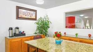 A kitchen with a granite countertop, wooden cabinets, a coffee maker, a potted plant, and a framed picture on the wall. - Americas Best Value Inn Irving Dfw Airport South (Irving)