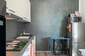 A compact kitchen with a microwave, a clock, and a small table with a tablecloth.