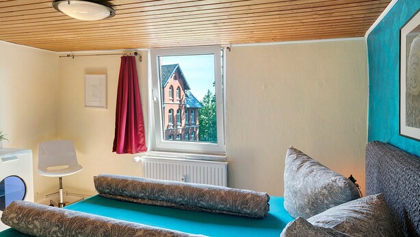 A room with a bed, a chair, a window with a view of a building, and a radiator.