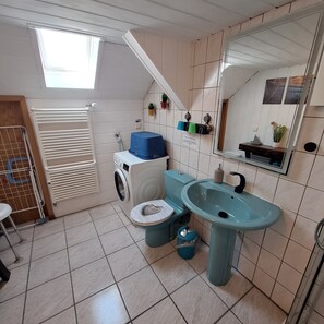 A compact bathroom with a washing machine, toilet, sink, and a skylight.