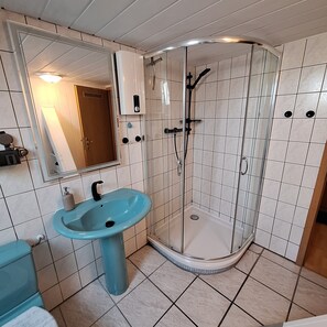 Un baño con lavamanos, espejo, ducha y paredes con azulejos.