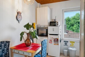 Une cuisine compacte équipée d’un four à micro-ondes, d’un four et d’un réfrigérateur, avec une horloge au mur et une fenêtre donnant sur un paysage verdoyant.