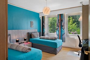 Une chambre avec deux lits, une fenêtre donnant sur un espace verdoyant, un radiateur et un bureau avec une chaise.
