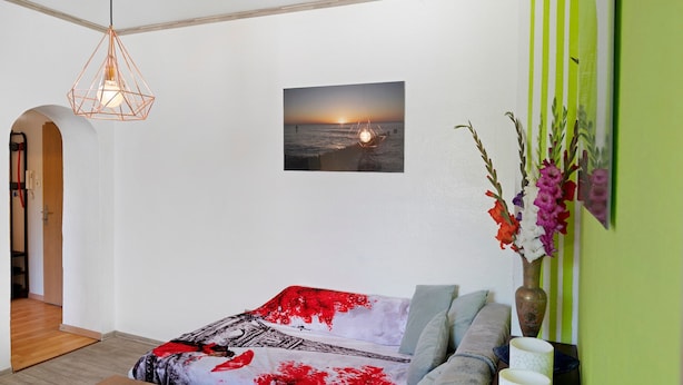 Una camera da letto con un letto, un lampadario, un quadro appeso al muro e un vaso con fiori.