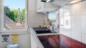 Una cucina con finestra, lavello e piano cottura. Si vedono cartelli per la raccolta differenziata e lo smaltimento dei rifiuti attaccati al muro.