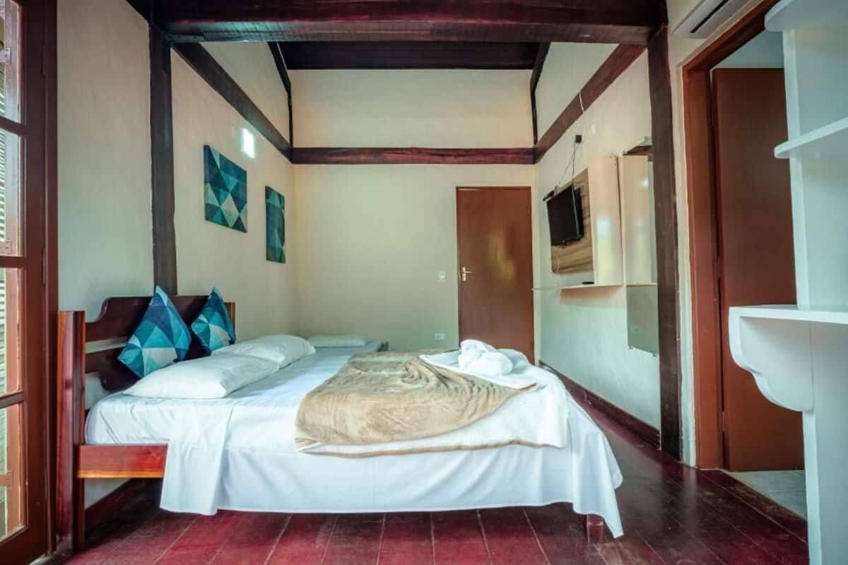 A room with a bed, a wooden headboard, a wall-mounted TV, a sink, and a door.