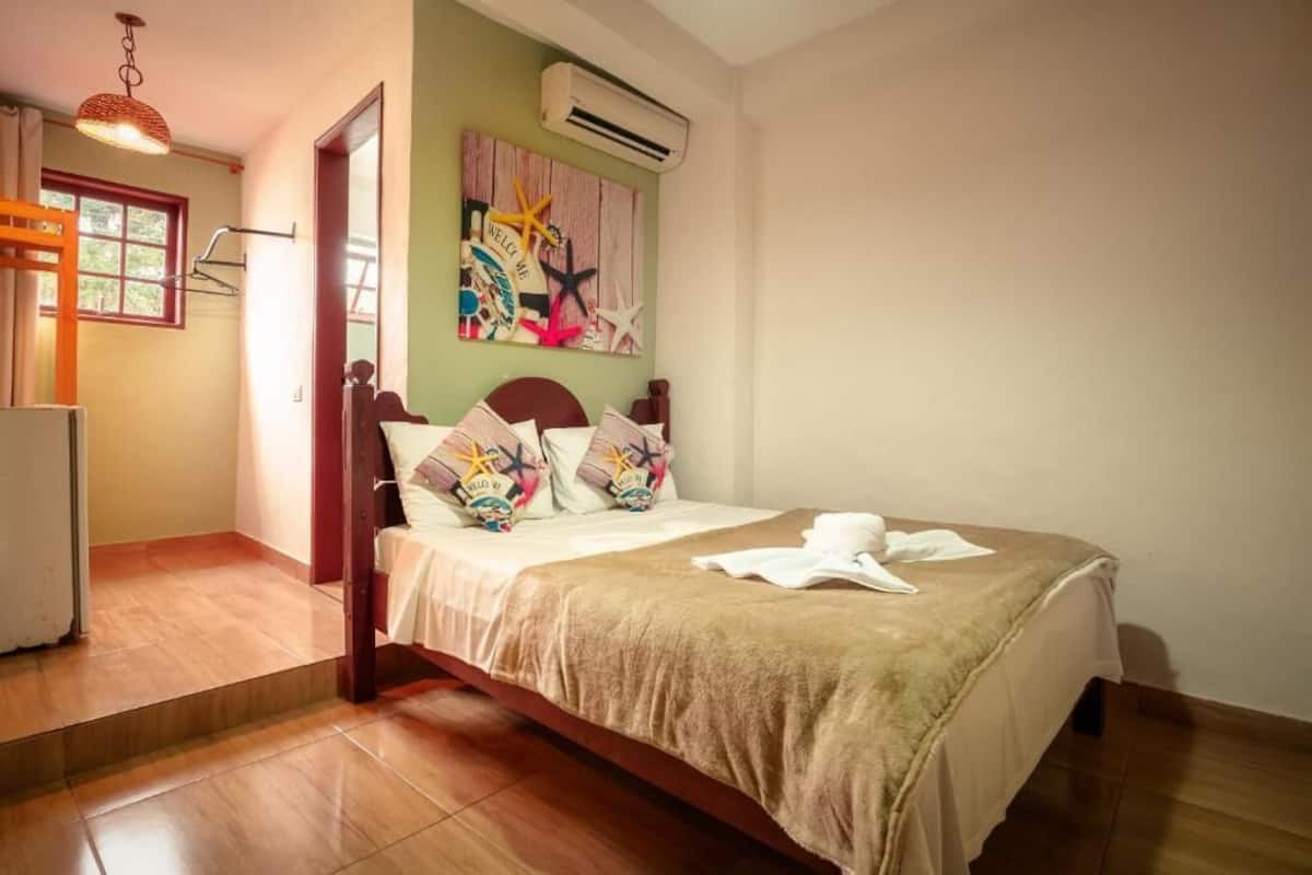 A bedroom with a bed, a wardrobe, a mirror, and a wall-mounted air conditioner.