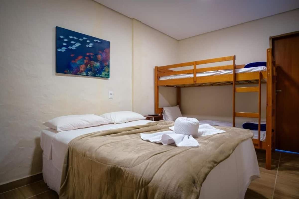 A room with a bunk bed, a single bed, a painting on the wall, and a door.