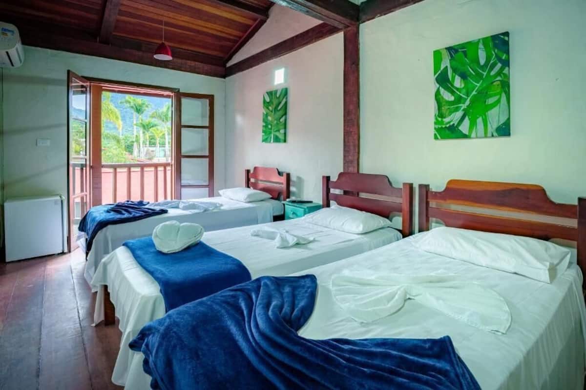 A room with two beds, a wooden ceiling, and a window with a view of palm trees.