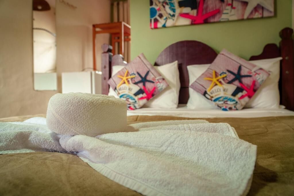 Una cama con una toalla blanca, un cabecero de madera y almohadones decorados con motivos de estrellas de mar.