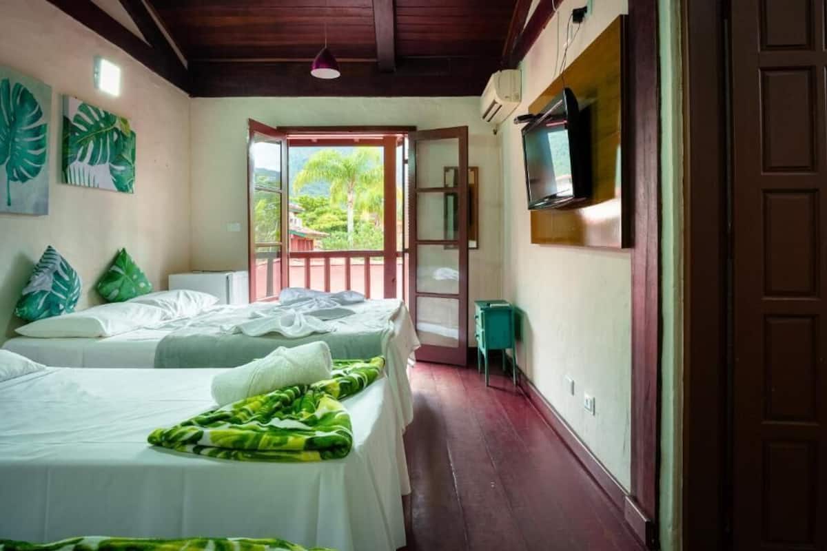 A room with two beds, a television, and a view of the outdoors.
