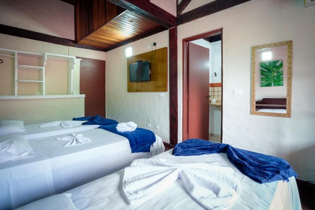A hotel room with two beds, a TV mounted on the wall, a mirror, and a door leading to another room.