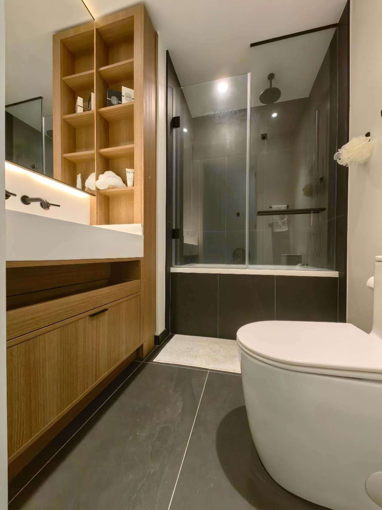 Et moderne badeværelse med et trækommode, en glasbadeværelsesafskærmning og et hvidt toilet.