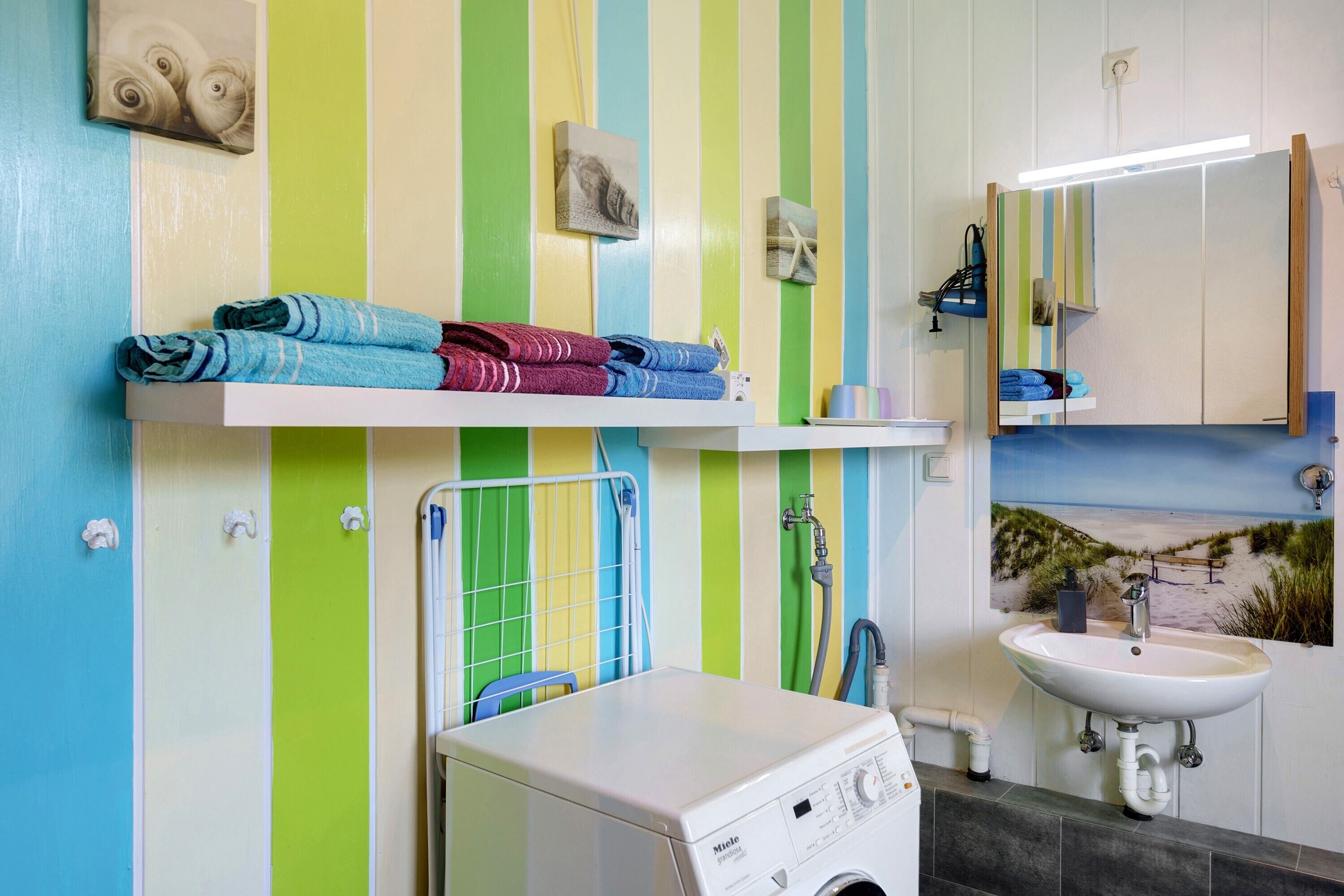 Une salle de bain avec un mur à rayures, un lave-linge, un évier et un miroir.