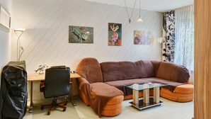A modern living room with a sectional sofa, a glass coffee table, a desk, and a chair. There are two wall-mounted paintings and a ceiling fan. - Spacious Apartment for up to 5 Guests (72 m²) in Hohenhameln (Hohenhameln)