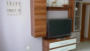 A modern room with a TV on a wooden stand, a white wall with a motivational quote, and a wooden wardrobe with a glass door. - Spacious Apartment for up to 5 Guests (72 m²) in Hohenhameln (Hohenhameln)