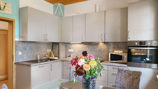 A modern kitchen with grey cabinets, a microwave, and a built-in oven. There is a vase with flowers on the counter. - Spacious Apartment for up to 5 Guests (72 m²) in Hohenhameln (Hohenhameln)
