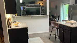 Une cuisine dotée d’un îlot central, de meubles de rangement sombres, d’un réfrigérateur et d’un coin repas avec des chaises.