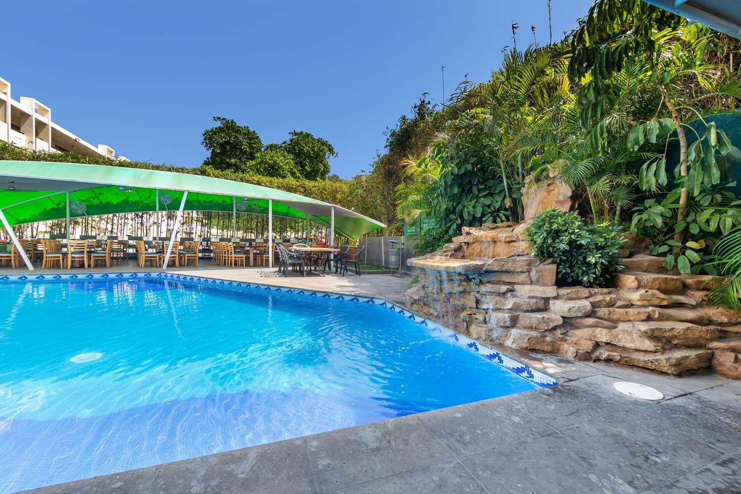 Una piscina con una cascada de piedra, rodeada de mobiliario de exterior y vegetación.