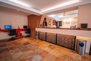 Uma área de recepção com balcão de check-in, computadores e um espelho grande.