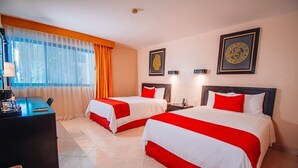 Habitación de hotel con dos camas, un escritorio, una silla y una ventana con cortinas.