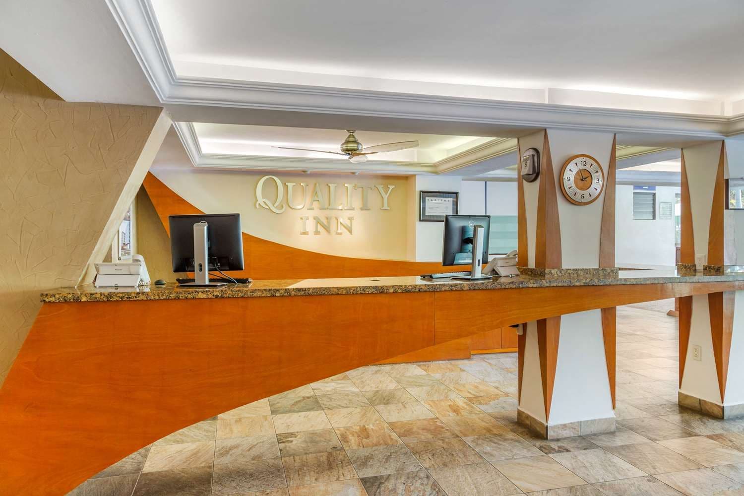 Una recepción con el letrero 'Quality Inn', un reloj y un ventilador de techo.