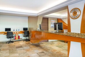 A reception area with a wooden reception desk, two computer monitors, and a clock on the wall. - Eco City Hotel (Tuxtla Gutierrez)