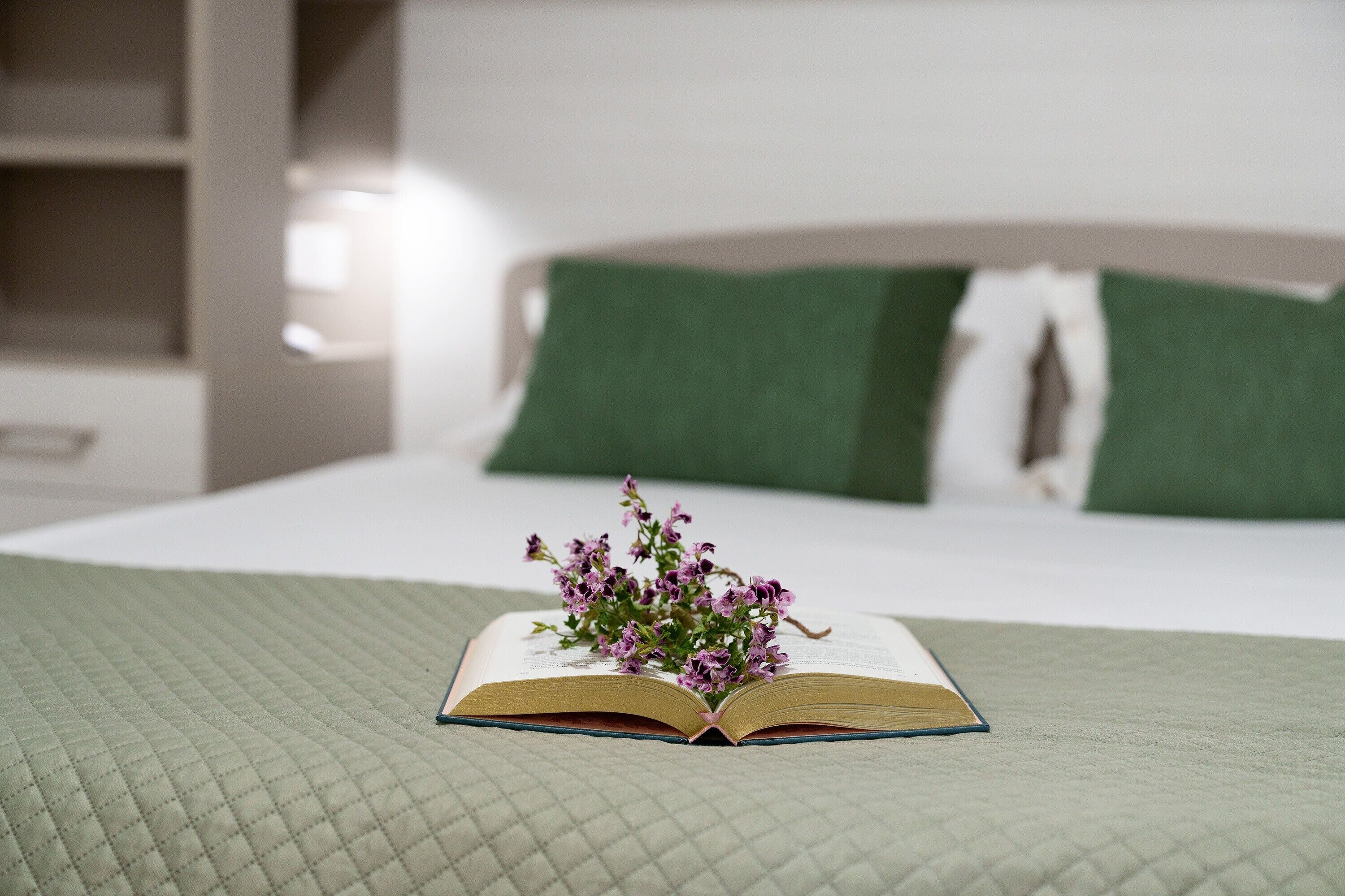 Een open boek met bloemen op een bed in een hotelkamer.