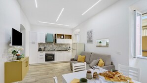 Una cucina moderna con mobili bianchi, un tavolo da pranzo con piano in vetro e un divano con cuscini.