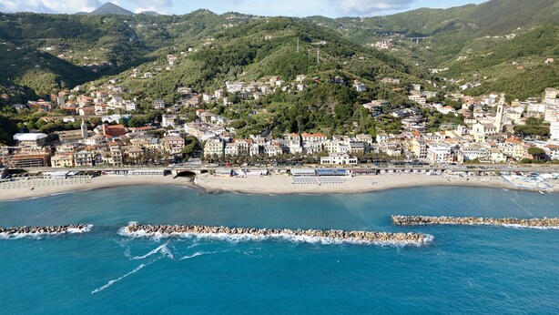 Una località costiera con una spiaggia, edifici e colline sullo sfondo.