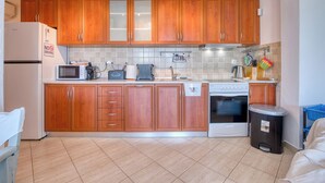 Une cuisine avec des meubles de rangement en bois, un four à micro-ondes, une cuisinière et une poubelle.
