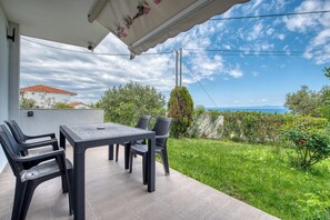 Patio esterno con tavolo e sedie, zona coperta e vista sul mare e sul verde.