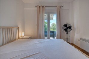 Una camera da letto con un letto, un comodino, una ventola portatile e vista sull'esterno tramite una porta scorrevole.