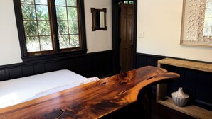 A room with a bed, a wooden table, a window, a door, and a wall-mounted decorative piece.