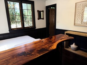 A room with a bed, a wooden table, a window, a door, and a wall-mounted decorative piece.