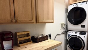 A kitchen with wooden cabinets, a coffee maker, a wooden tray, and a stacked washer and dryer.