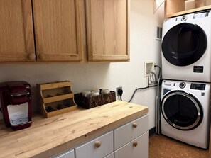 A kitchen with wooden cabinets, a coffee maker, a wooden tray, and a stacked washer and dryer.