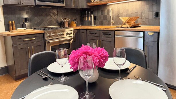 A modern kitchen with dark cabinetry, a microwave, stove, and a dining table set with plates and glasses.