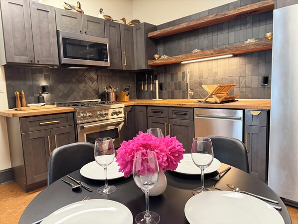 A modern kitchen with dark cabinetry, a microwave, stove, and a dining table set with plates and glasses.